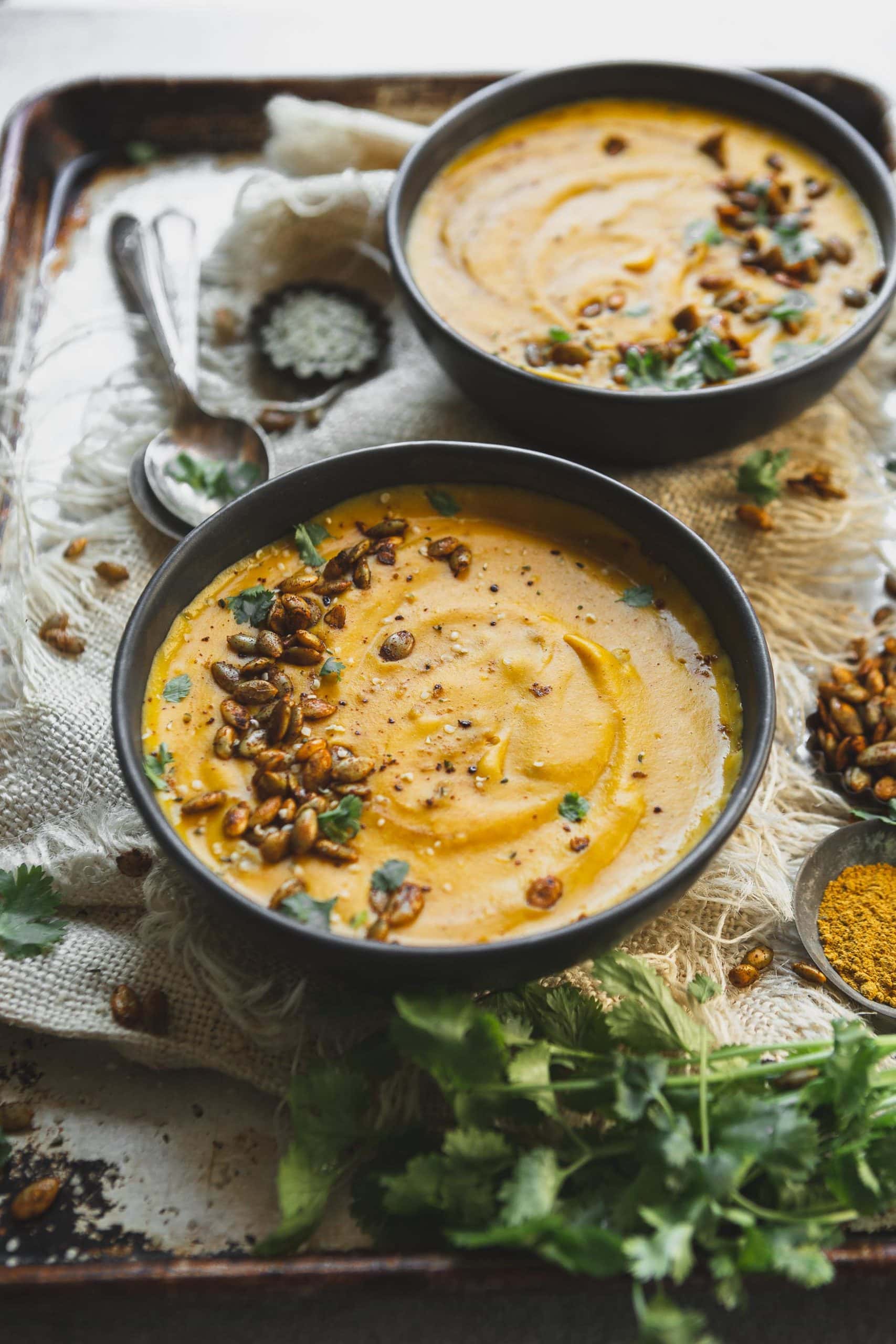 A bowl of vegan butternut squash soup topped with cilantro and hemp seeds. Another bowl of soup is in the background.