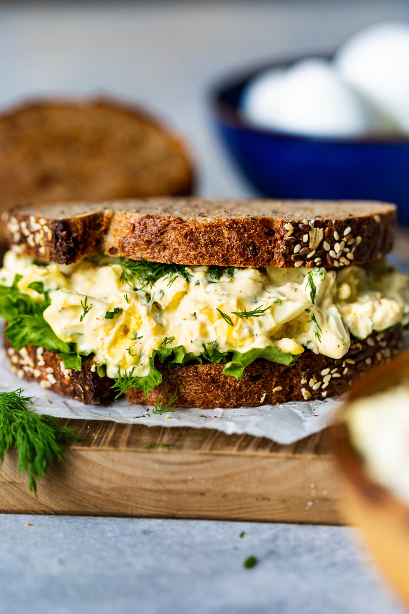 a photo of an egg salad sandwich piled high with egg salad filling, a piece of lettuce all between two slices of toasted 7 grain bread.