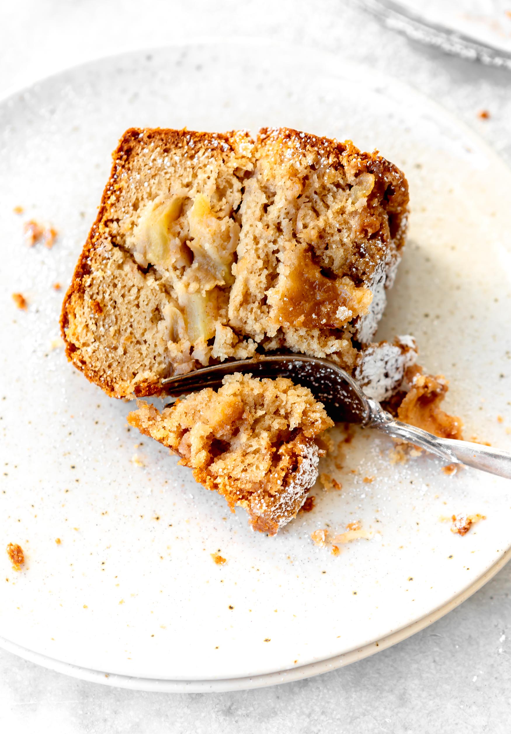 A slice of Jewish Apple cake on a white dessert plate. The cake is dense and moist with apple slices in it.