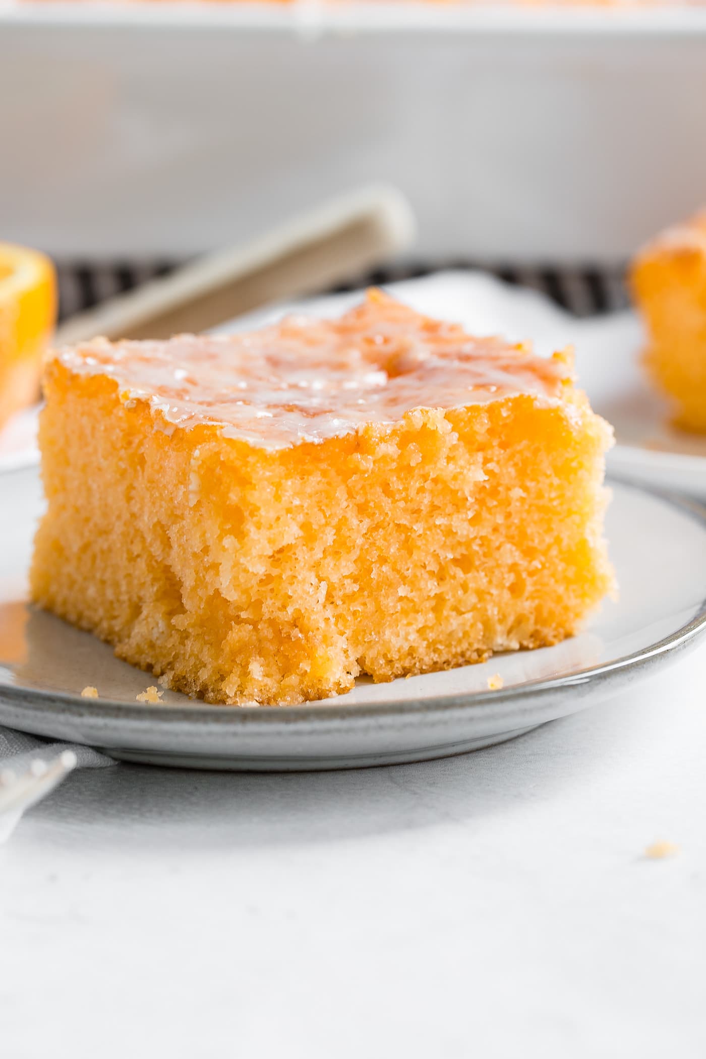 A photo of a piece of orange jello cake on a small white plate with orange glaze on the top.