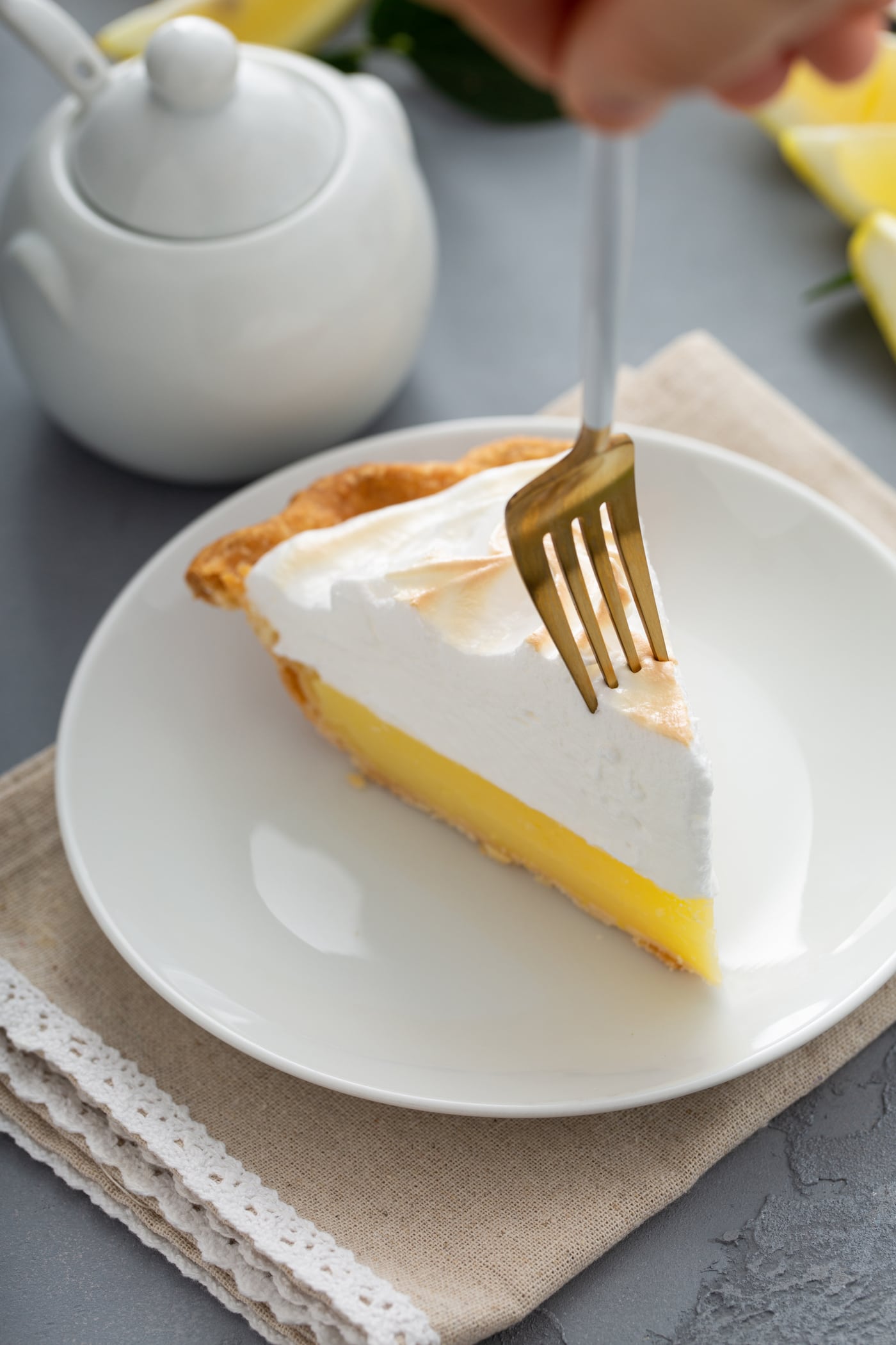 A piece of lemon meringue pie. A fork is piercing the tip of the slice.