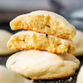 a photo of thick and soft sugar cookies piled on each other. the top cookie has been broken in half and stacked on each other with the center facing the camera.