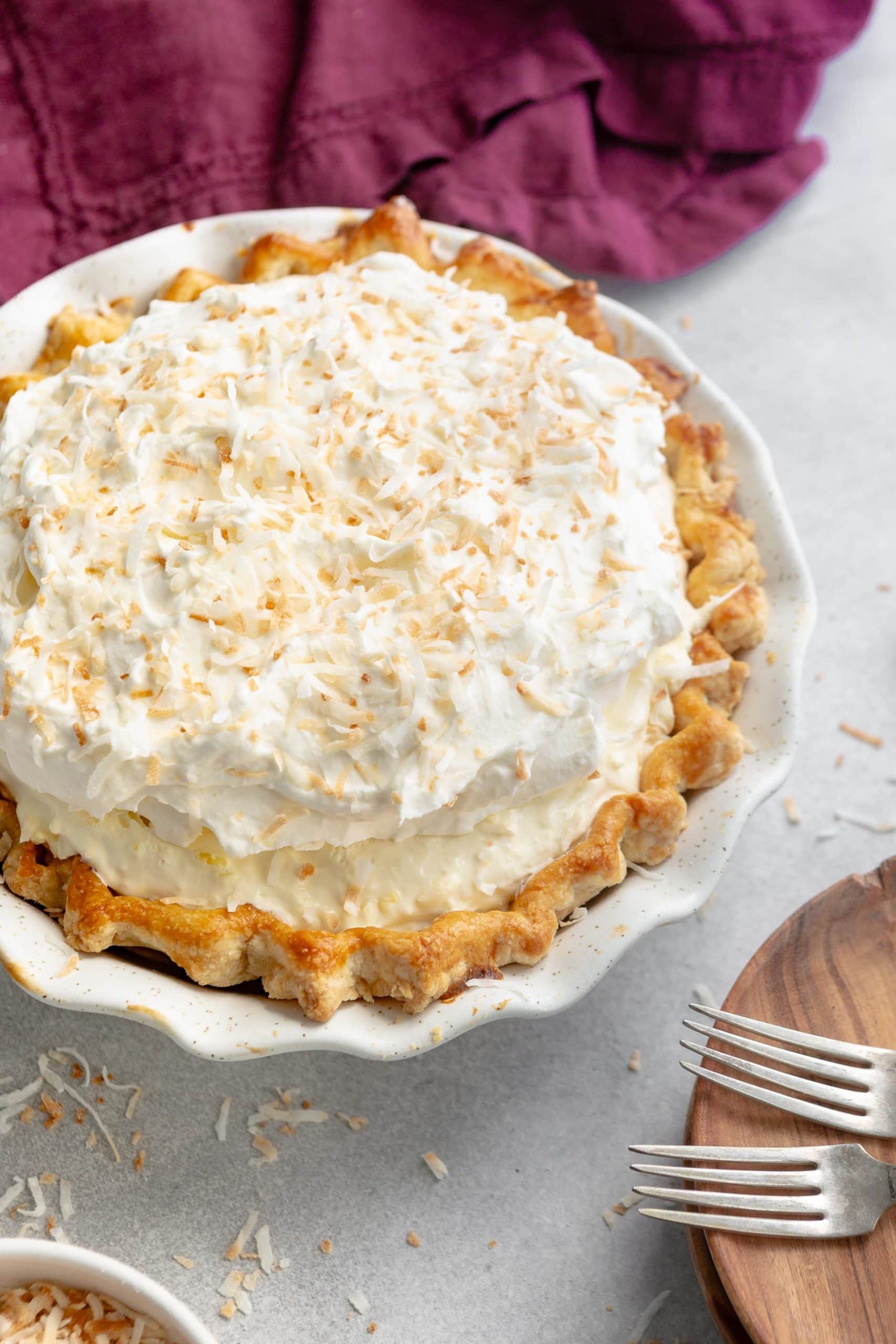 a photo of a whole coconut cream pie topped with toasted shredded coconut with a golden homemade crust in a white ceramic pie dish.