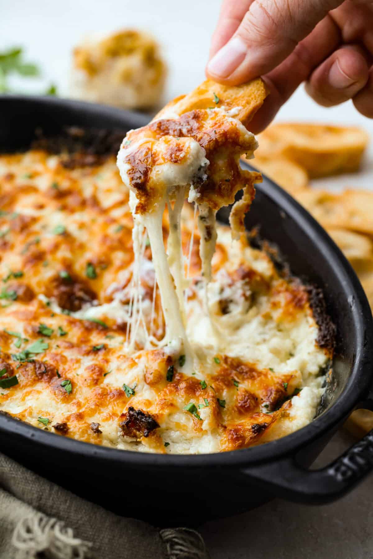 Someone puling up a cheesy bite of garlic bread dip with a crostini. 