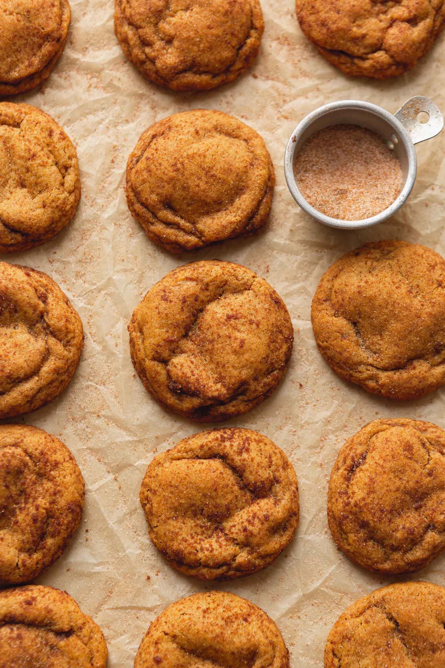 Three rows of chewy pumpkin cookies with a small bowl of cinnamon sugar. The cookies are baked and look soft and chewy.