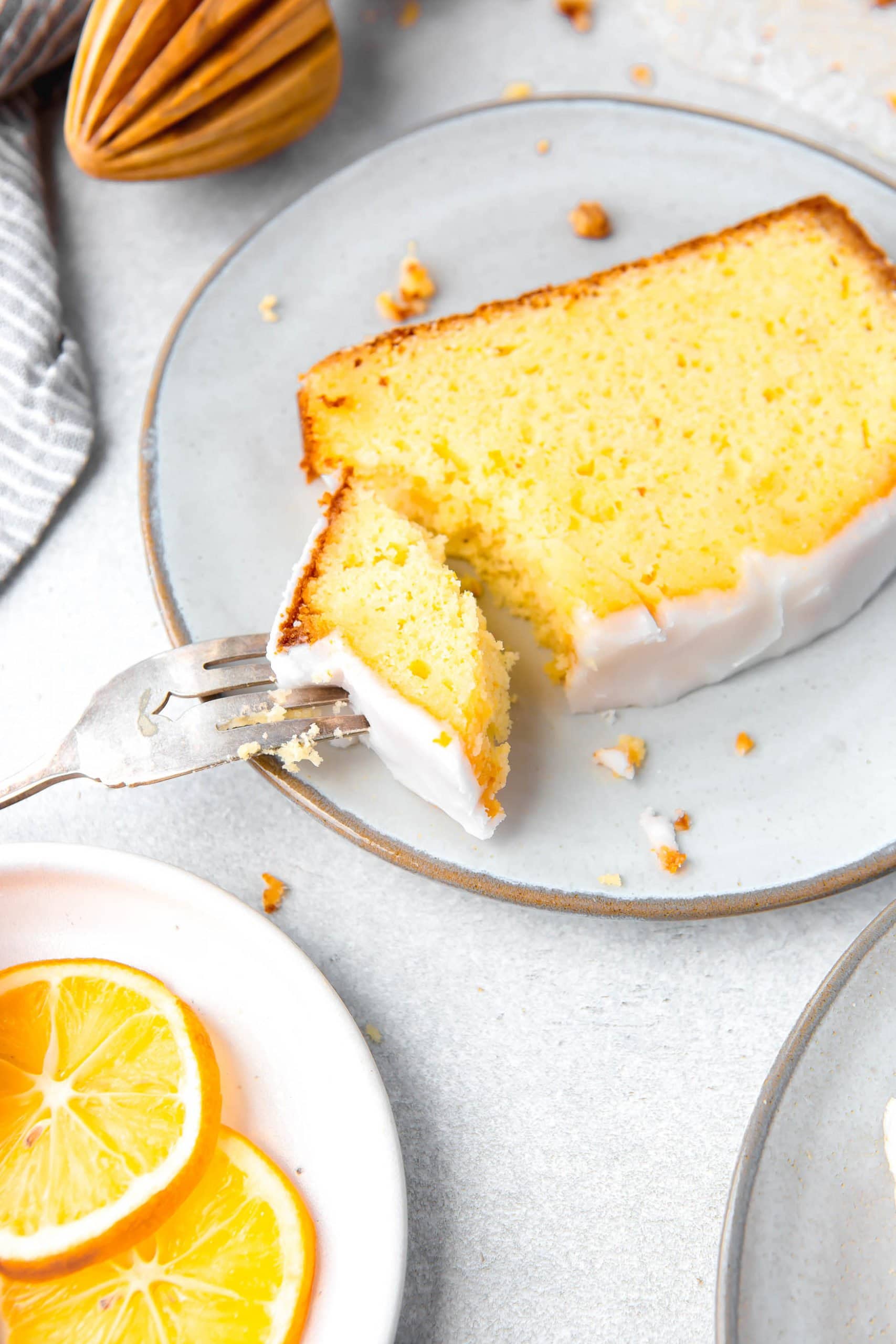 a photo of a slice of lemon loaf cake sitting on a white plate with a piece being taken out with a silver fork.