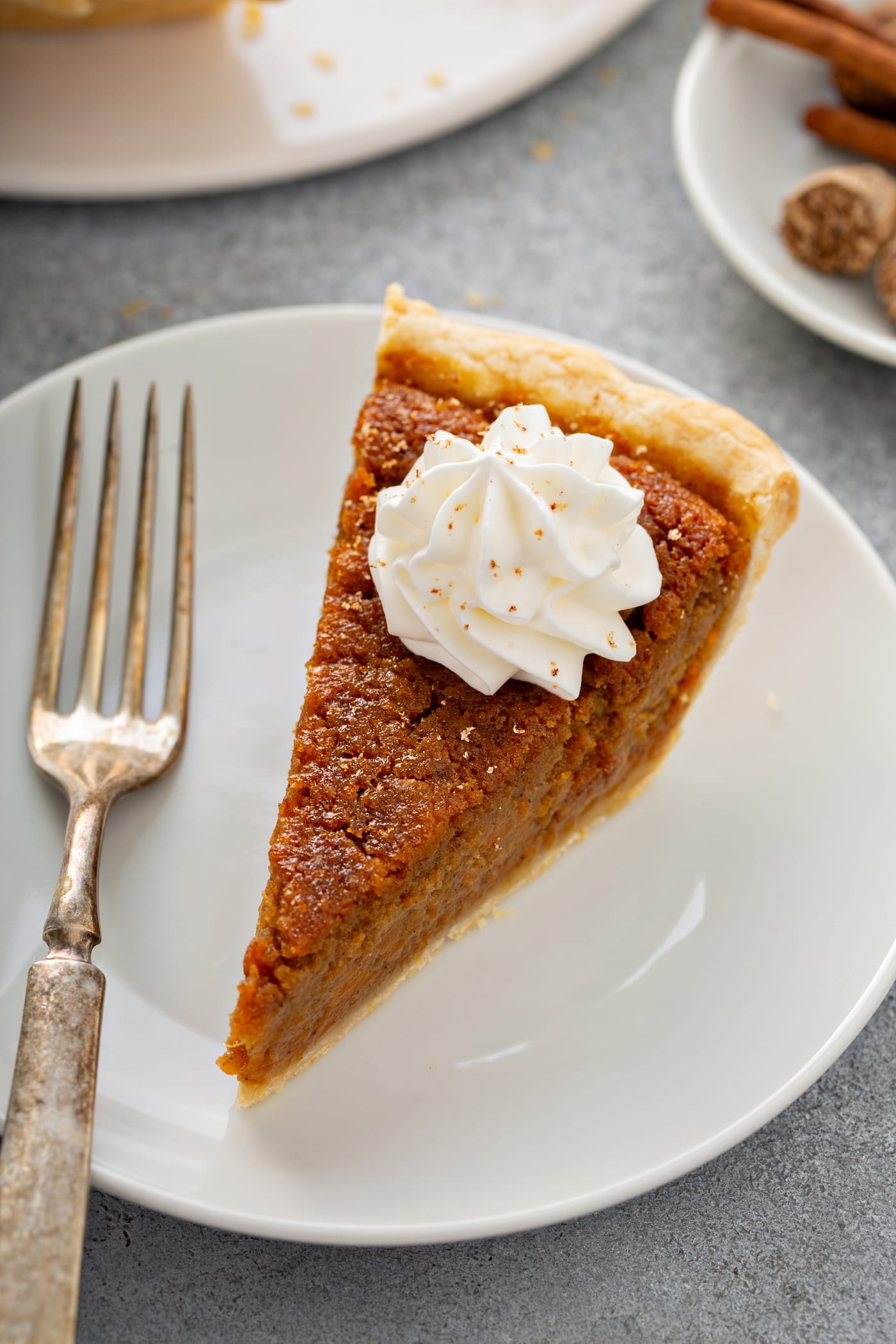 A photo of a slice of sweet potato pie sitting on a white plate with a silver fork sitting next to it.