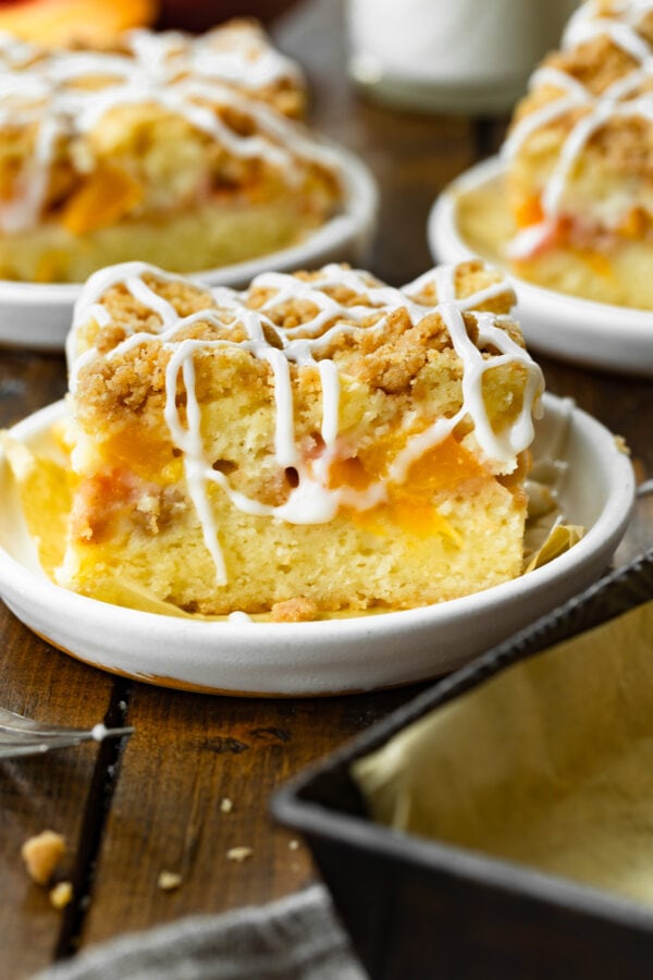 a photo of a piece of peach coffee cake topped with a streusel topping and a creamy white drizzle.