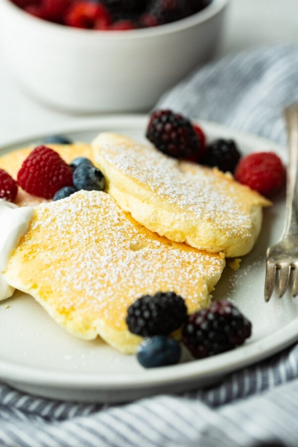 a photo of three fluffy Japanese cloud pancakes topped with powdered sugar and mixed fresh berries