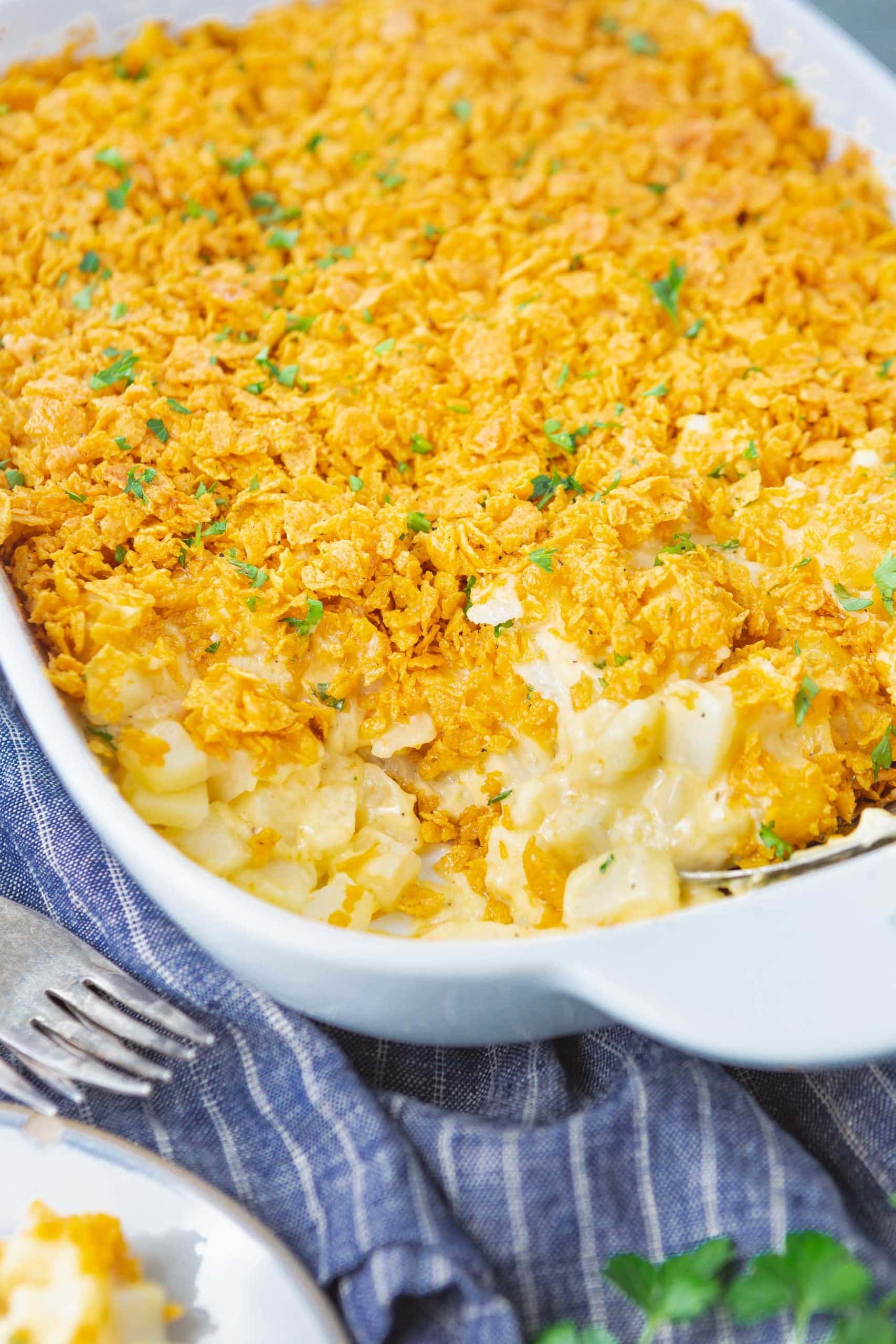 a photo of a casserole dish full of cheesy potato casserole with a serving in the corner of the dish removed.