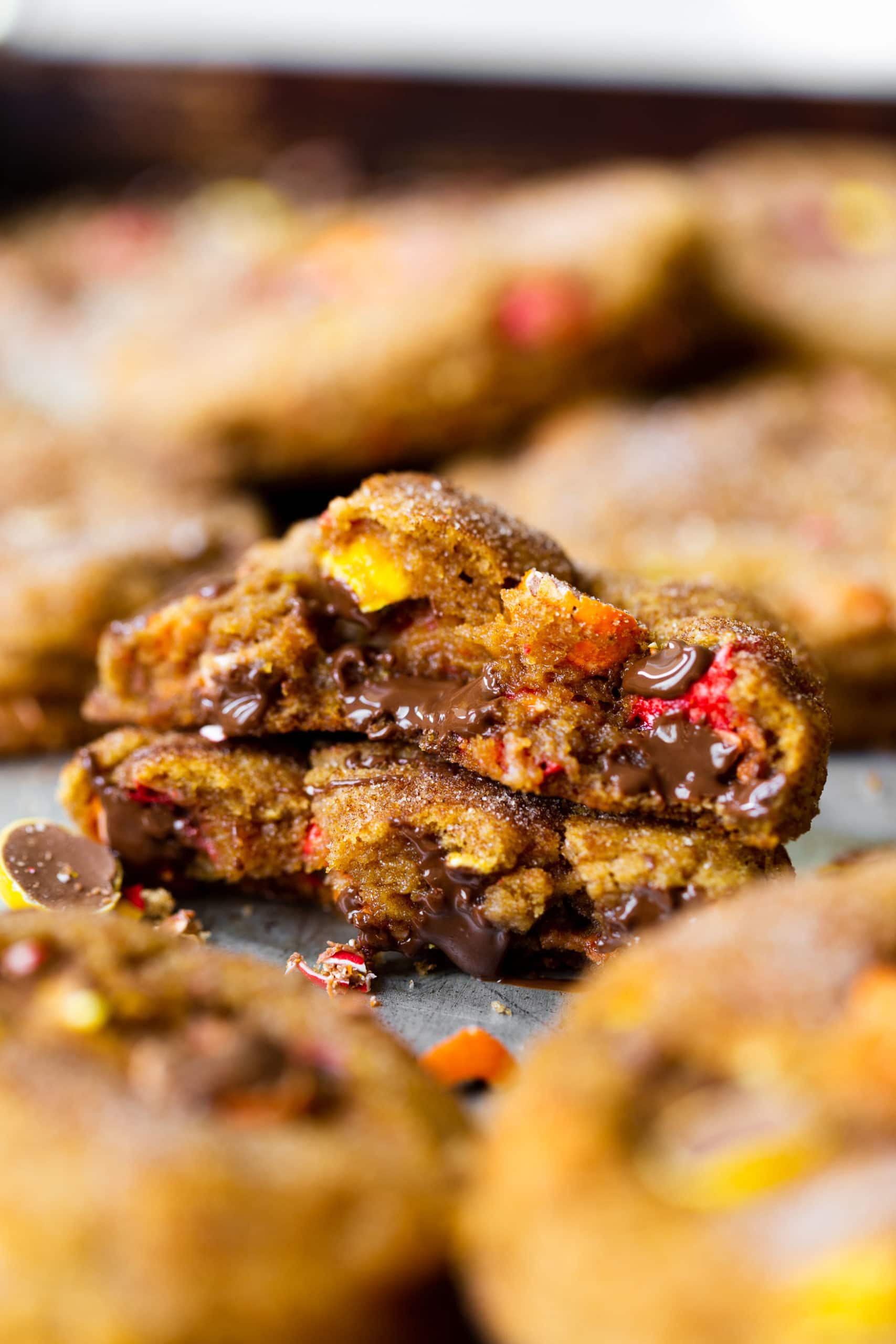 a photo of a pumpkin cookie full of cadbury chocolate bits. the cookie has been broken in half and the two halves are stacked on each other with the center facing the camera.