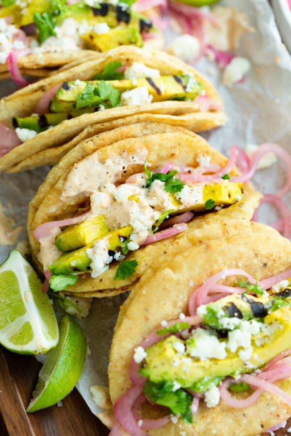 a photo of grilled avocado tacos topped with pickled red onions, crumbled queso fresco and a lime crema.