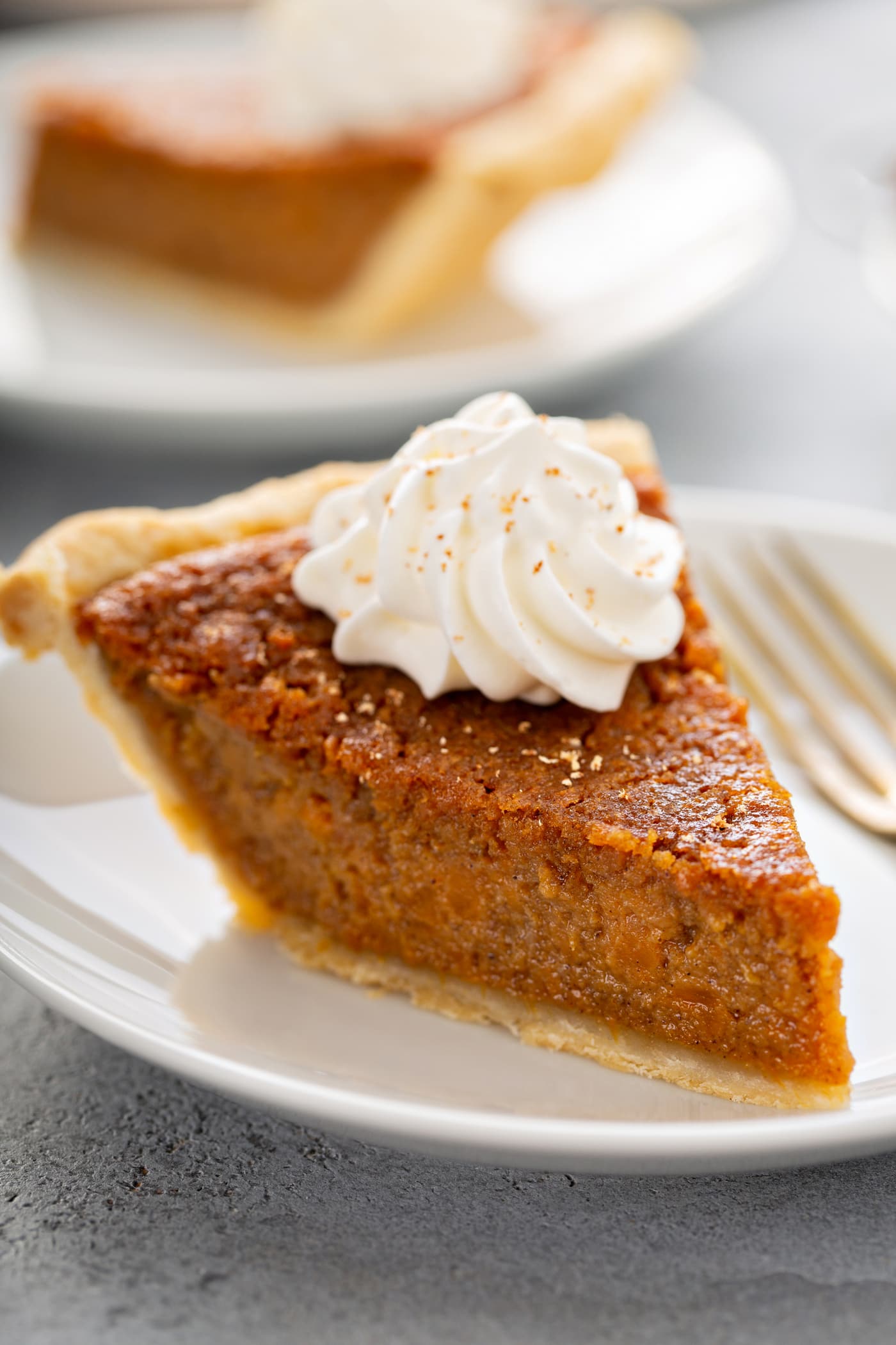 A photo of a slice of sweet potato pie with a dollop of whipped cream on top sitting on a white plate.