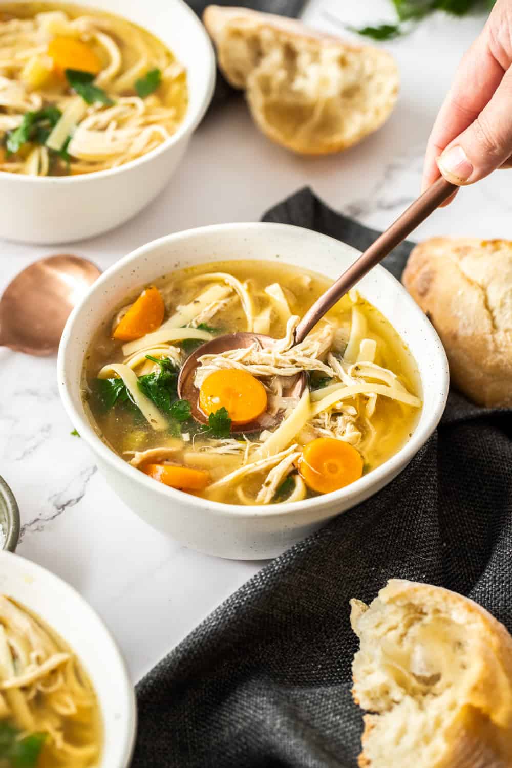 A white bowl filled with chicken noodle soup and a spoon digging in