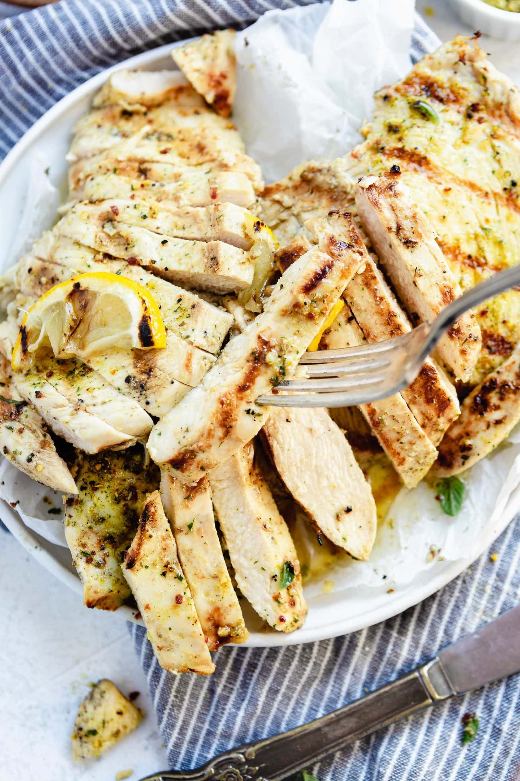 Sliced grilled chicken breast with a fork piercing a slice of chicken.