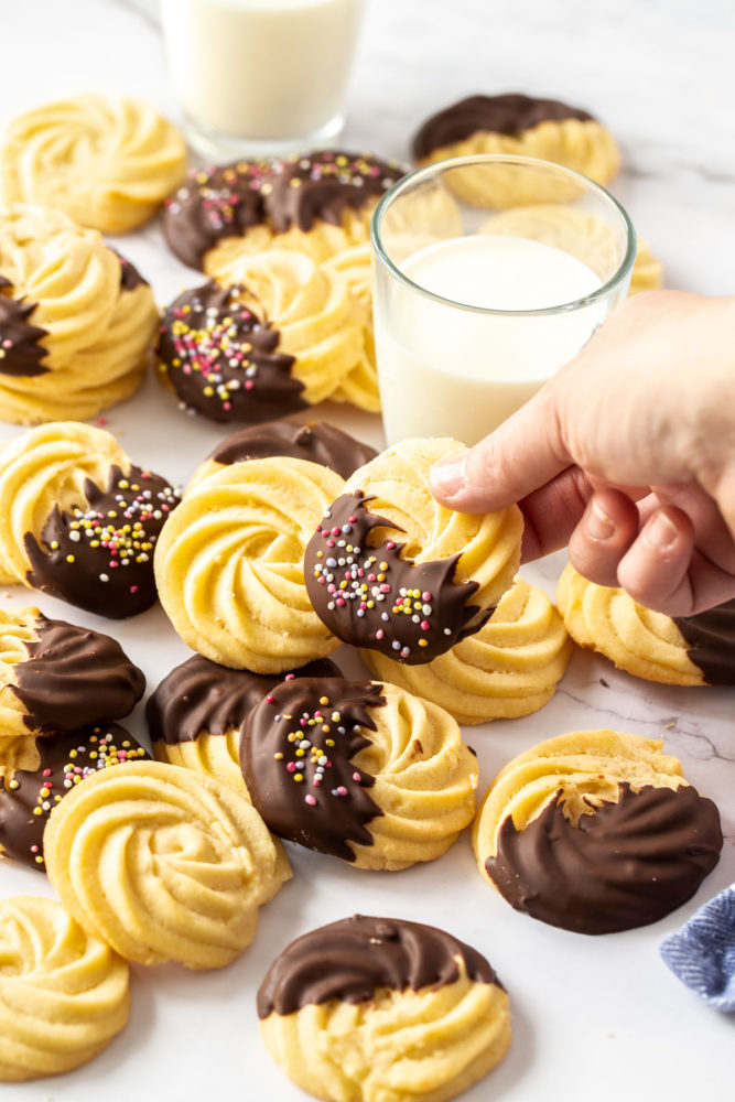 A batch of butter cookies, some chocolate coated. One being picked up