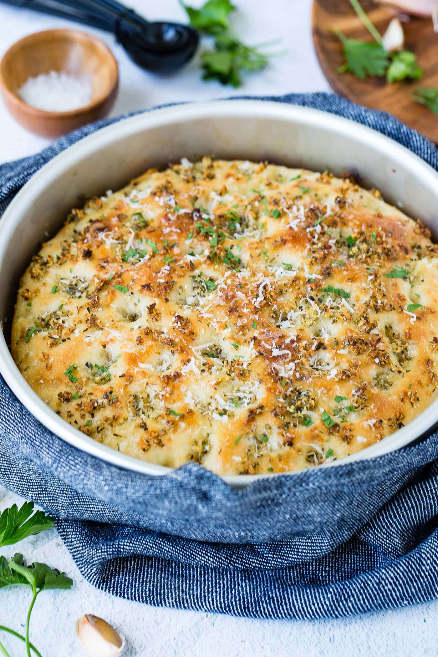 A baking dish with freshly baked Garlic Parmesan focaccia bread. It is golden brown with bits of green herbs.