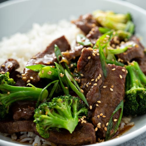 A close up of broccoli beef on a plate next to white rice.