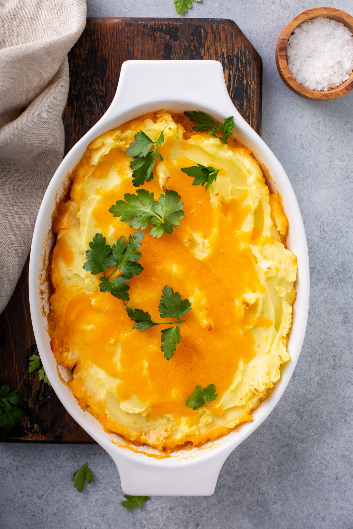 A casserole dish containing a baked shepherd's pie. It is topped with melted cheese and parsley leaves.