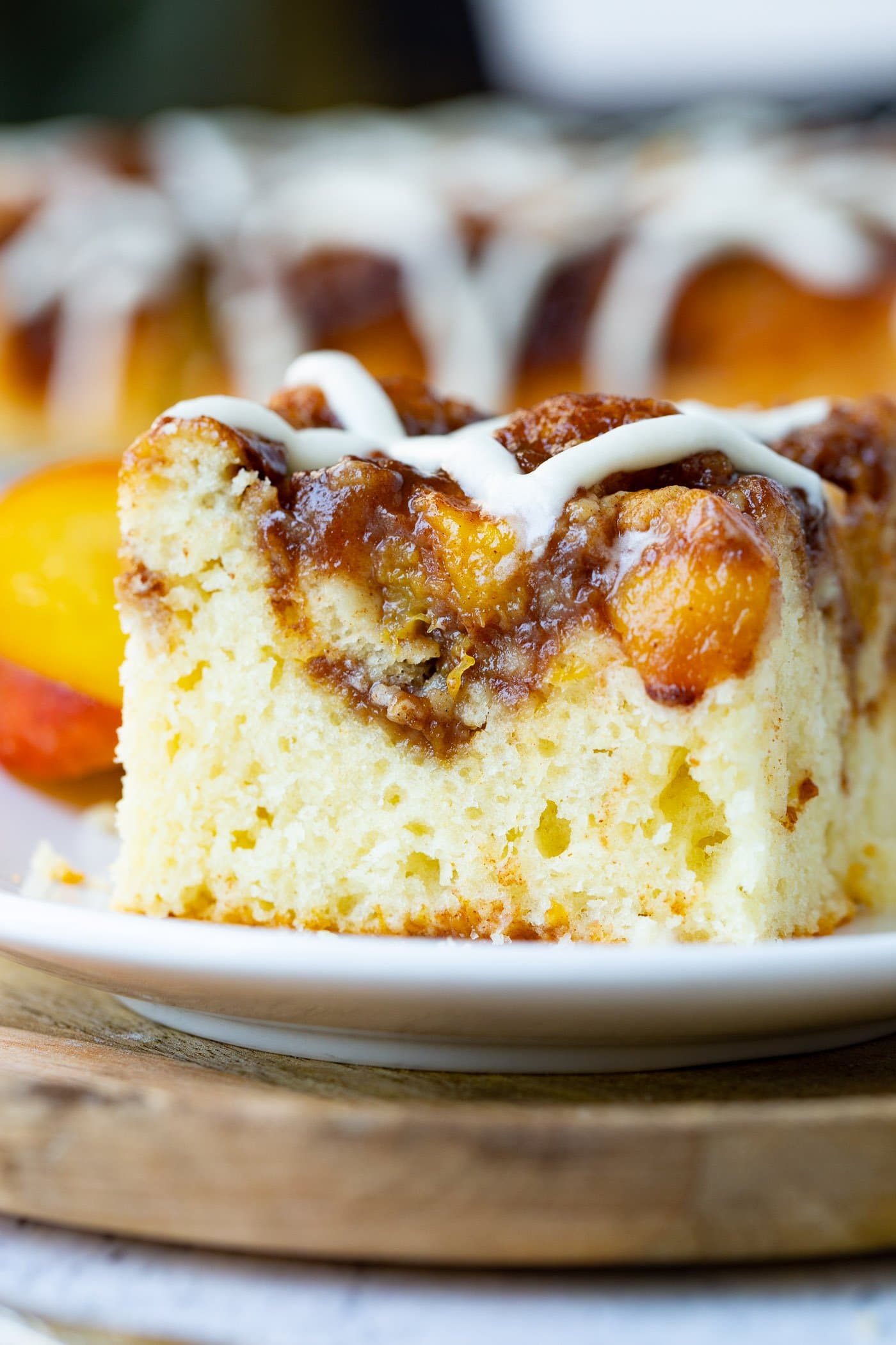 a piece of coffee cake topped with a brown sugar peach topping and sweet glaze sitting on a small white plate on top of a wooden board.