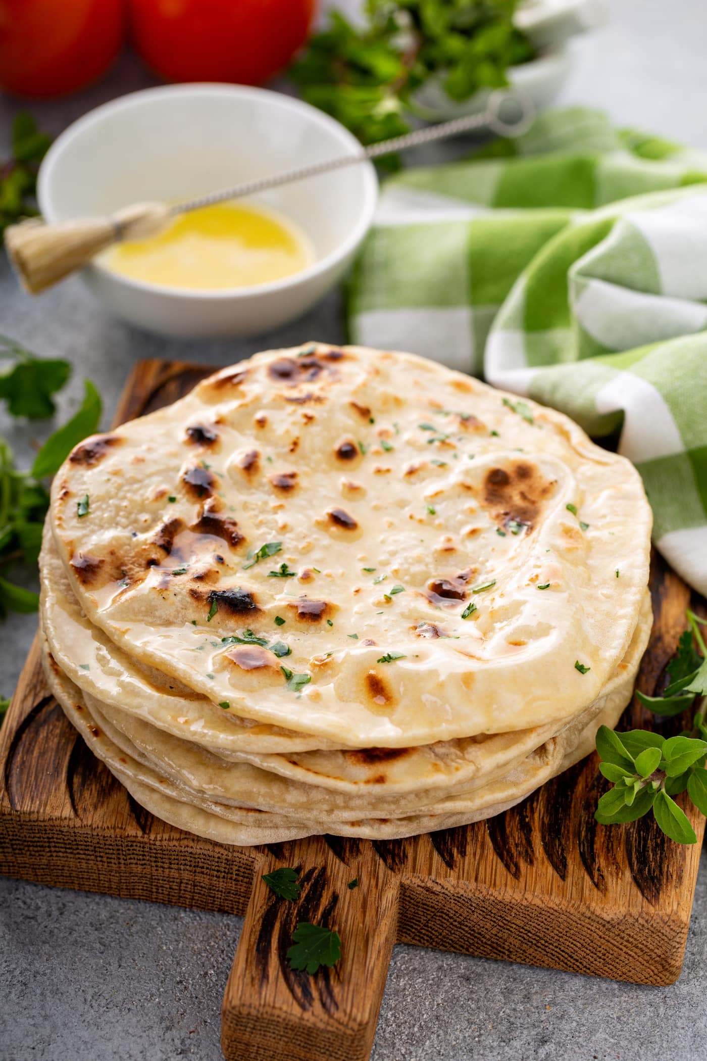 A photo of a stack of cooked discs of unleavened bread topped with chopped fresh herbs.