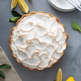 A picture of a lemon meringue pie. the meringue is fluffy and slightly browned. There are lemon wedges next to the pie.