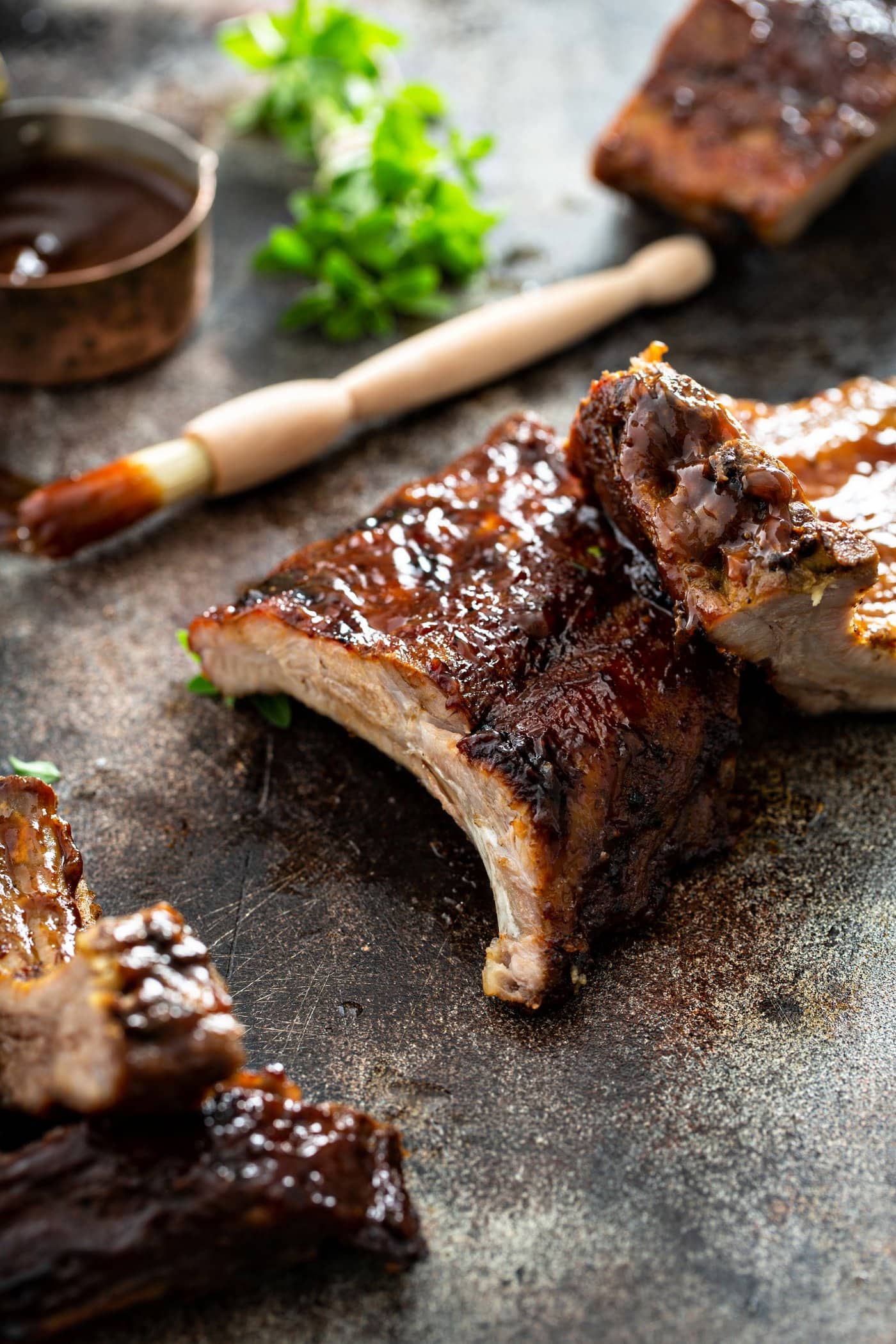 A rack of grilled pork ribs with a couple of ribs that are sliced off. A brush with glaze and a measuring cup of rub and some fresh thyme are in the background.