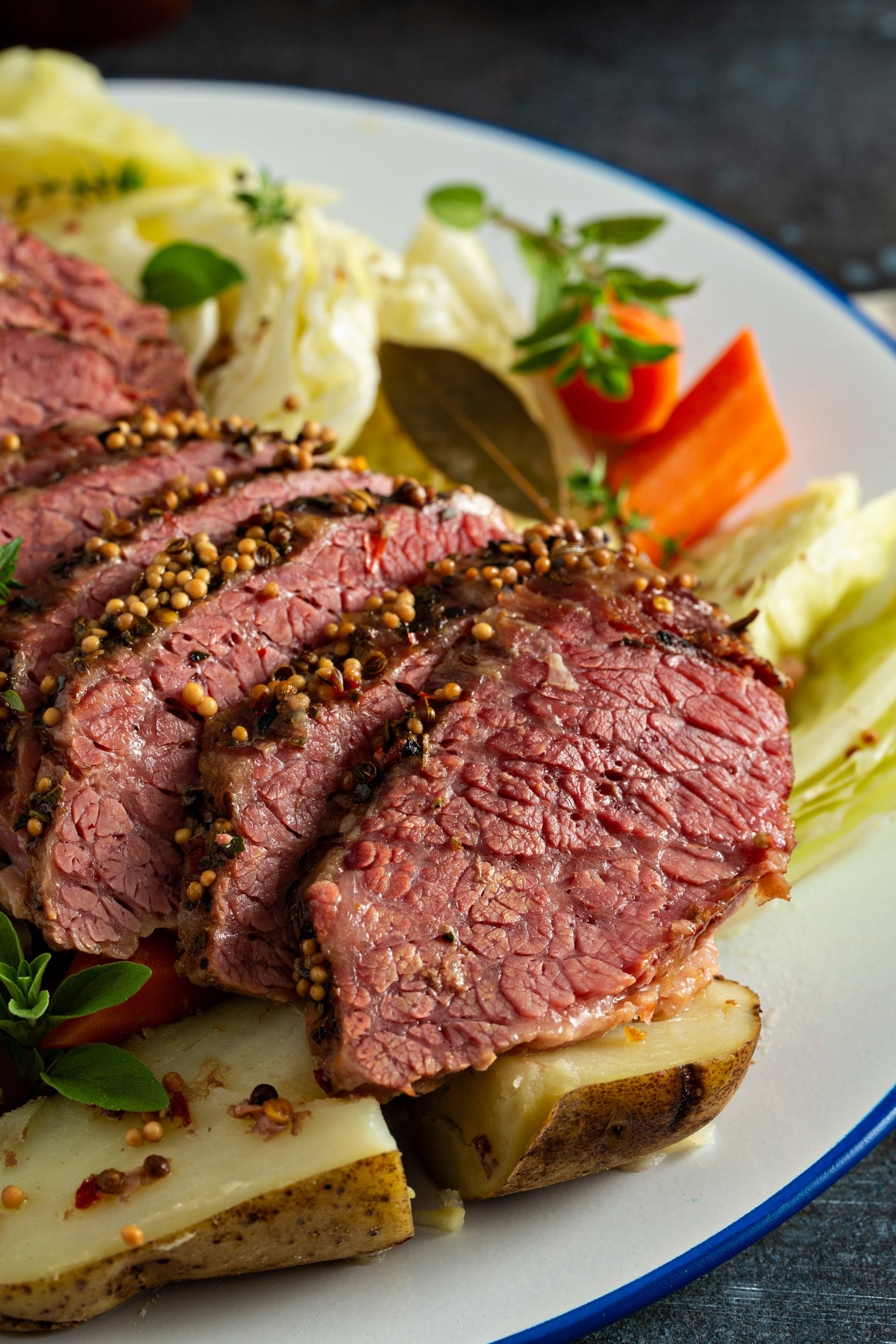 Slice corned beef resting on top of cabbage, potatoes and carrots with sprigs of herbs on the side.