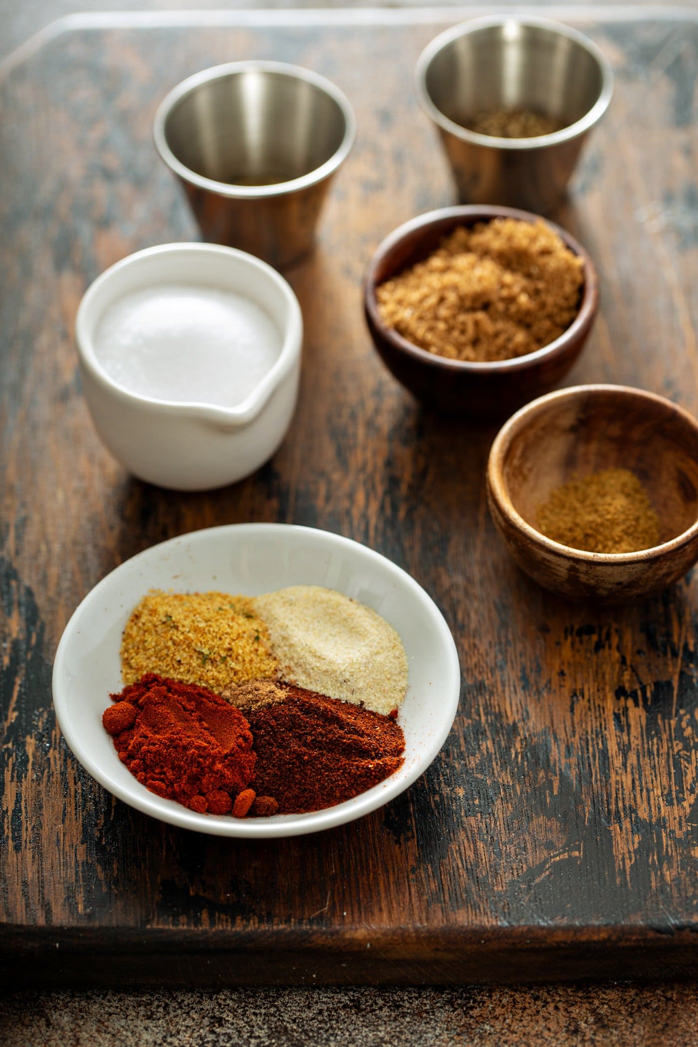 Ingredients for the rub for grilled bbq ribs. little containers of paprika, onion powder, garlic powder, and cumin. a container of salt, a little bowl of brown sugar, thyme and nutmeg.