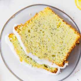 a photo of two slices of lemon poppy seed loaf cake stacked on a plate. the two slices are topped with white icing.
