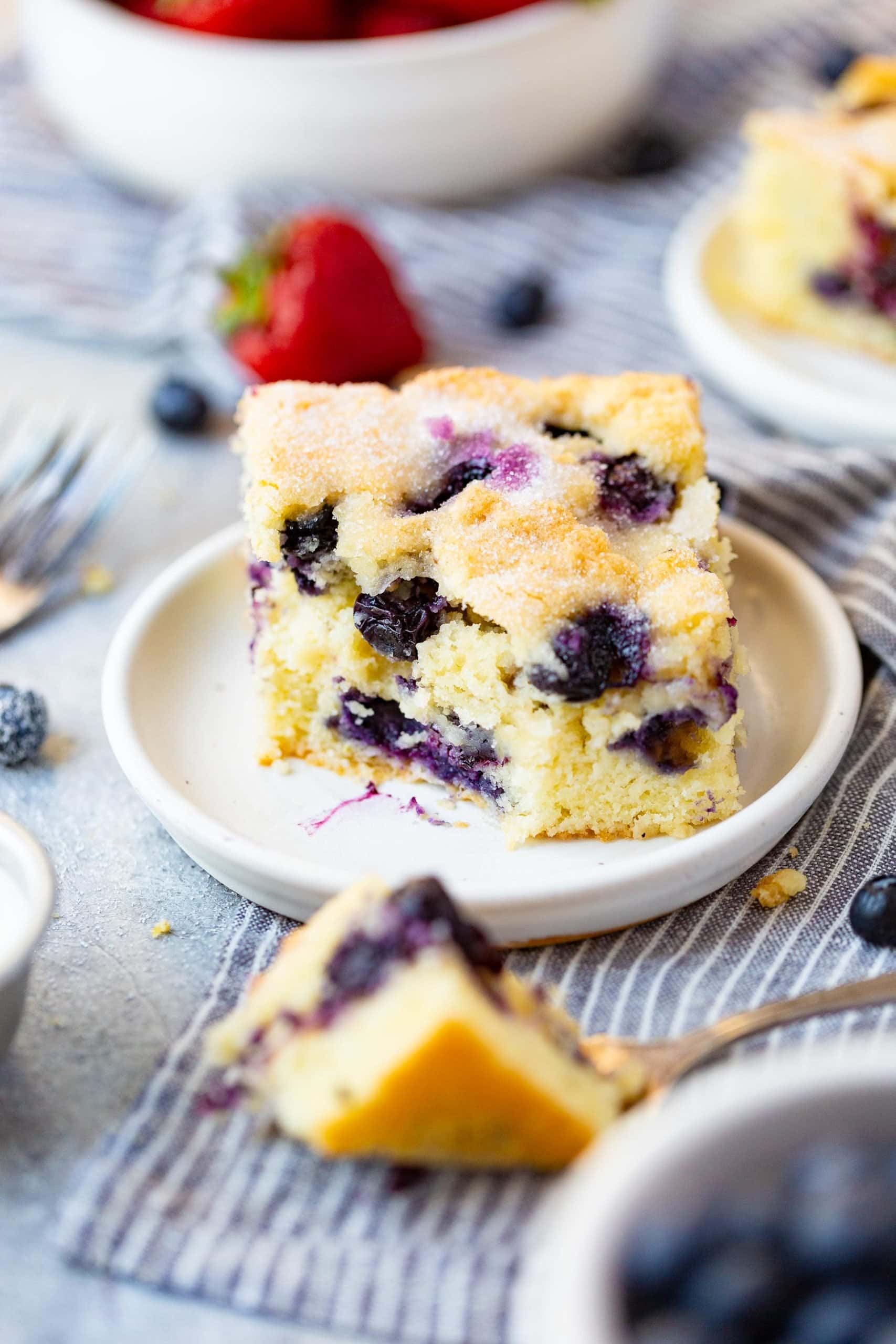 a photo of a piece of blueberry breakfast cake with a bite taken out of it. the bite is sitting on a fork in the foreground.