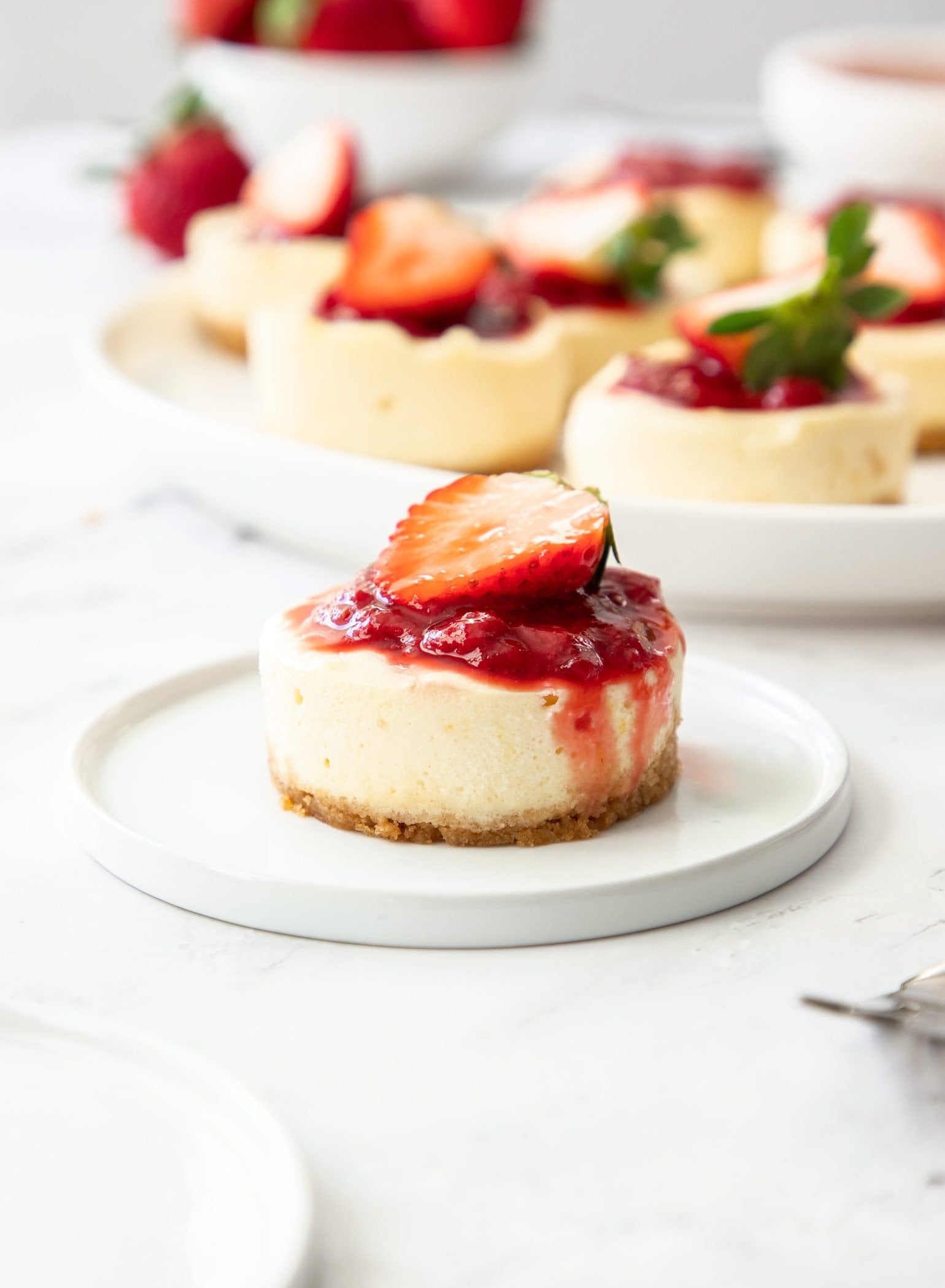 A mini cheesecake on a small white plate, with more in the background