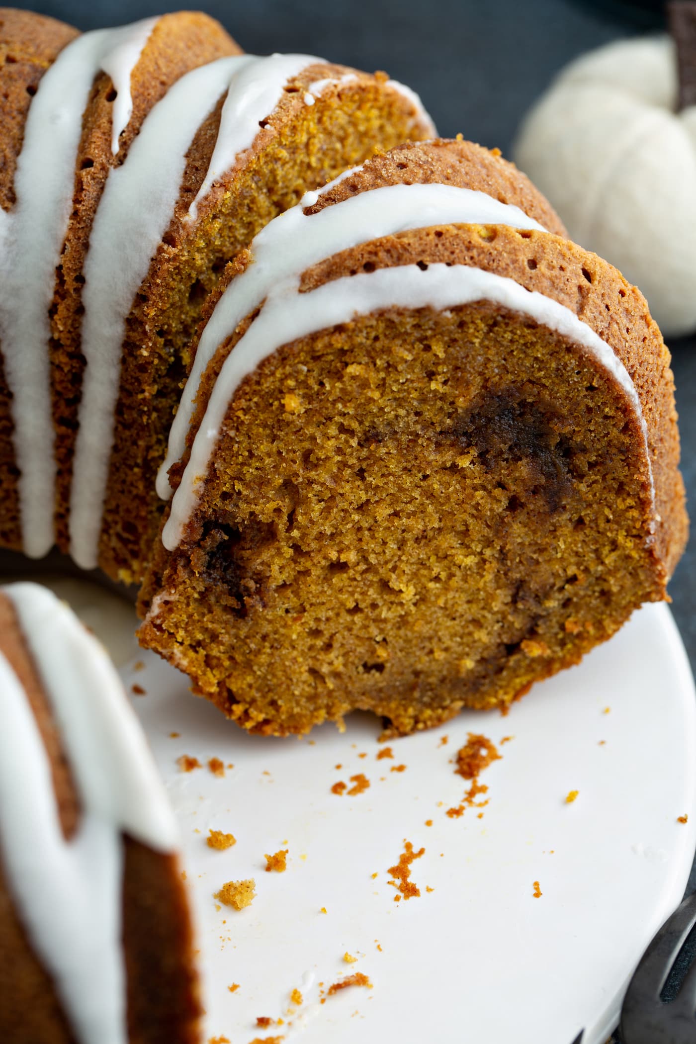 A close-up picture of a sliced sour cream cinnamon swirl pumpkin bundt cake. The cake is drizzled with white glaze and you can see the cinnamon swirl in the middle of the cake.