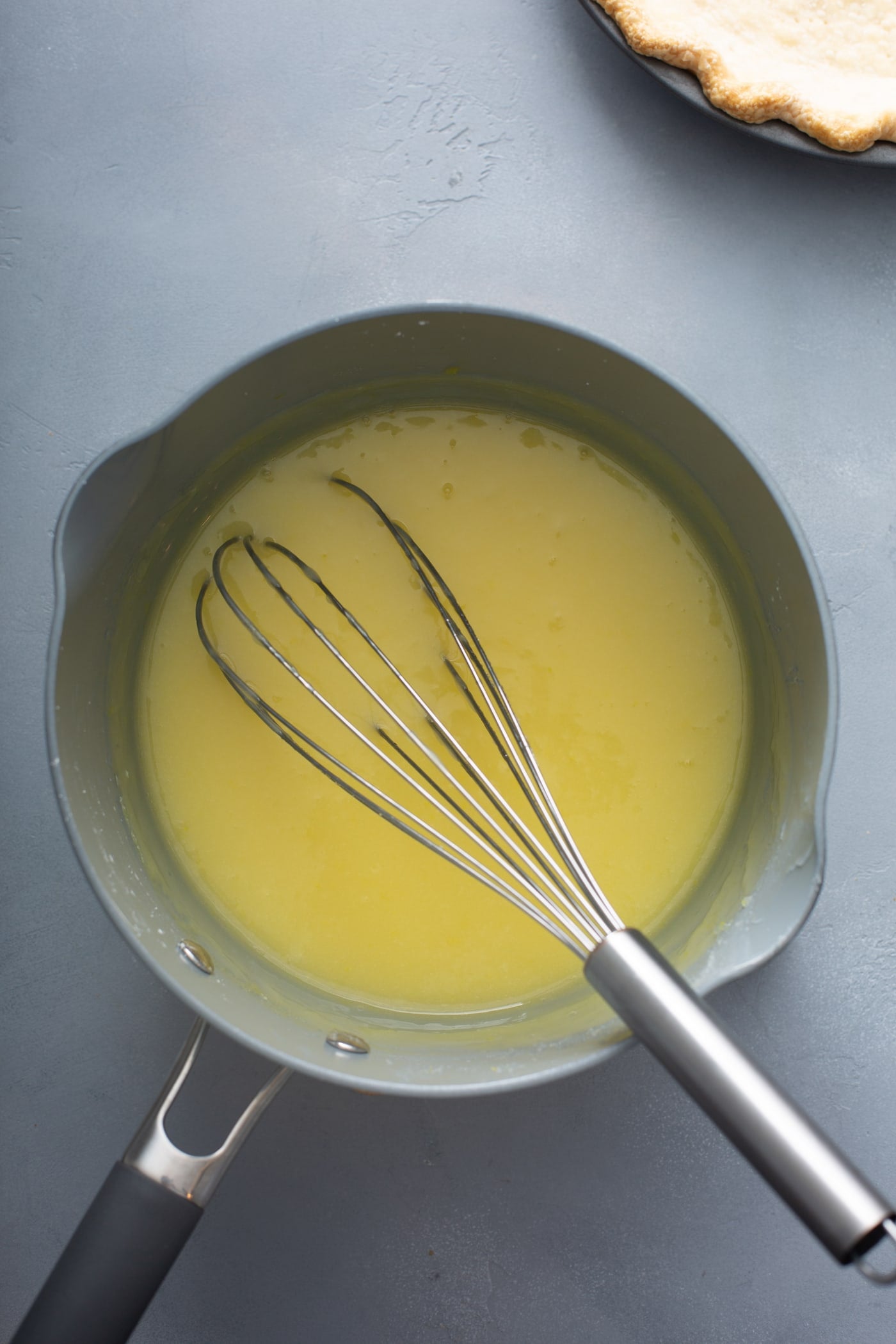 A picture of a sauce pan with lemon pie filling. A whisk is in the pan.