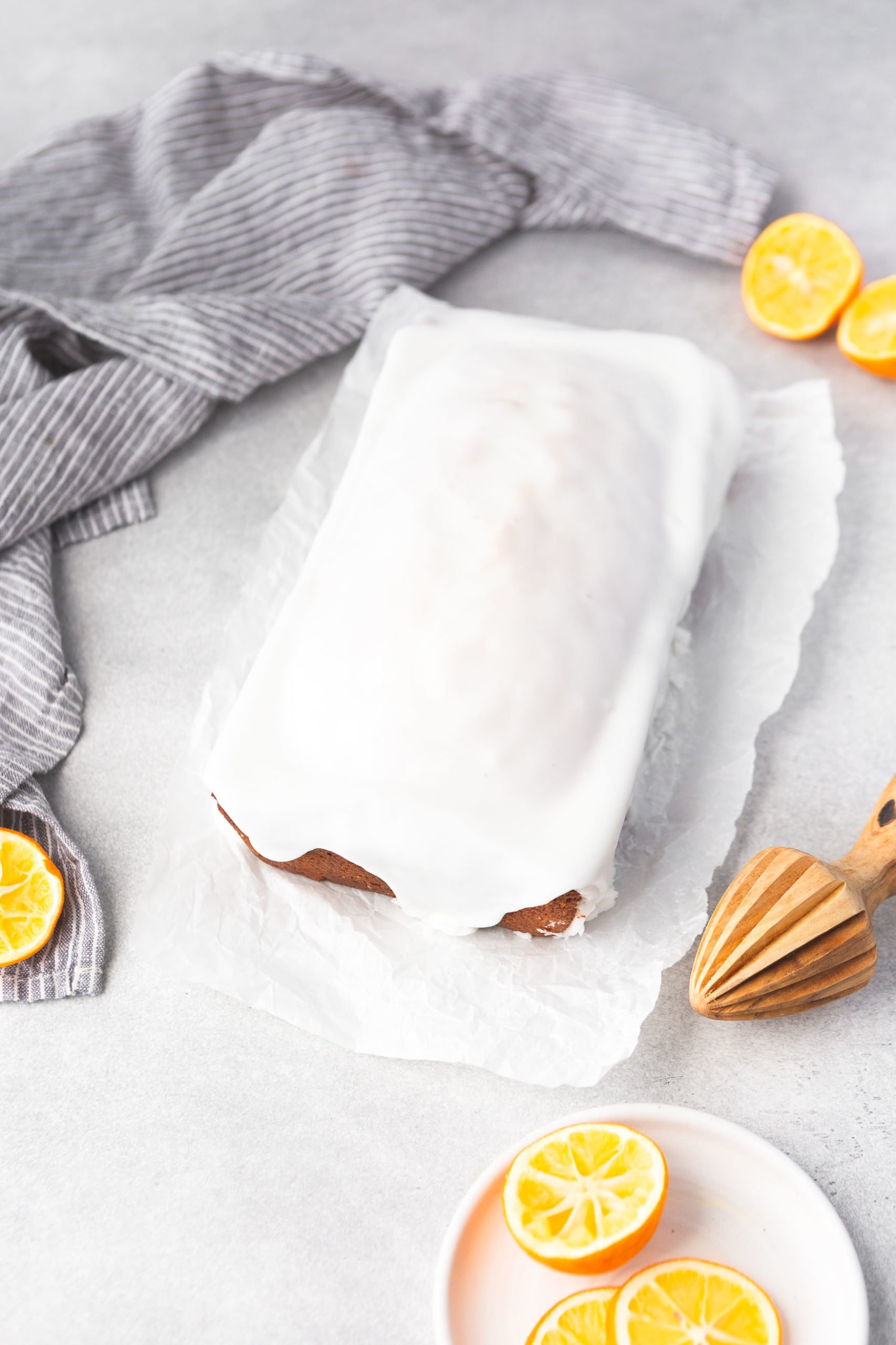a photo of a lemon loaf cake covered in white icing. the loaf is sitting on a piece of parchment paper.