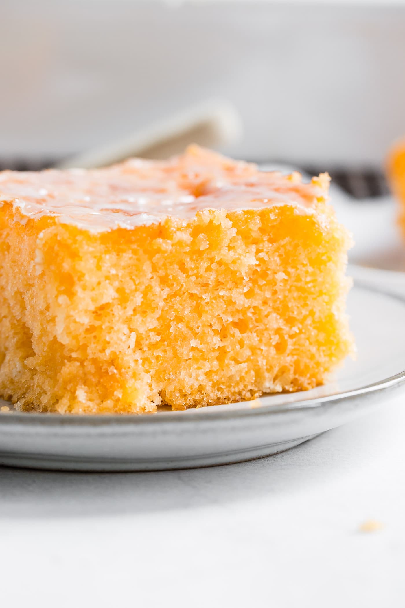 A closeup photo of a piece of orange jello cake on a small white plate.
