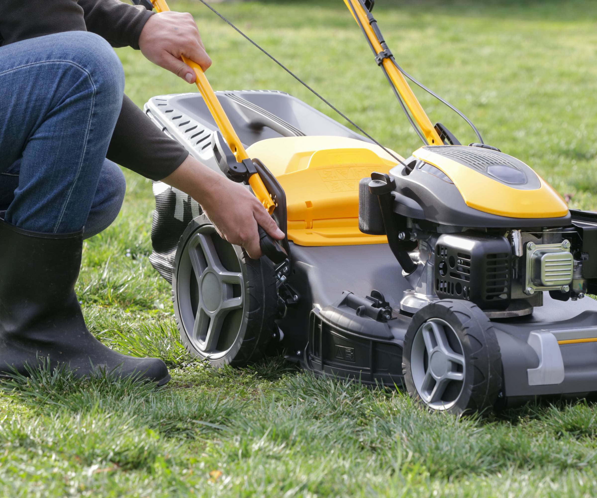 A person adjusting the mowing height of a black and yellow lawn mower