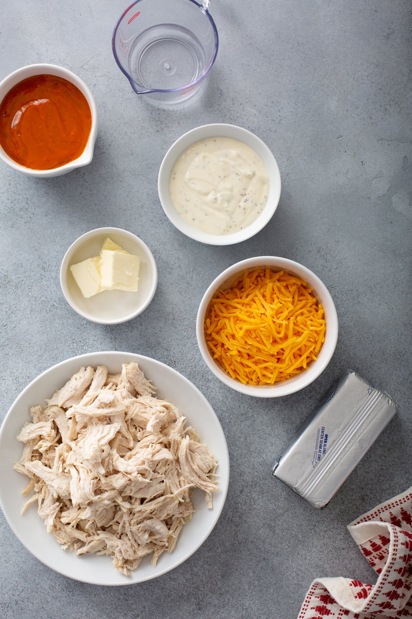 Small containers of shredded chicken, cheese, hot sauce, ranch dressing and butter.