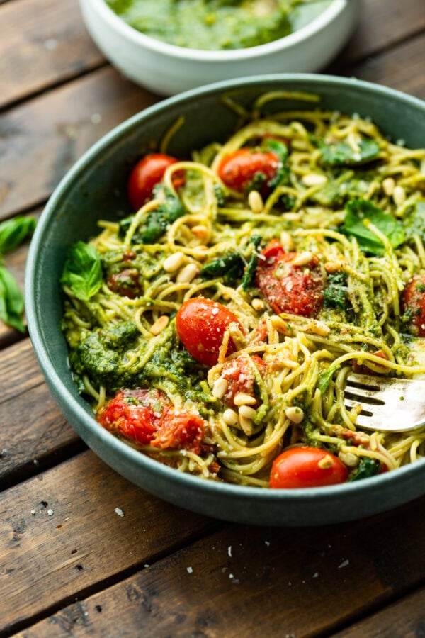 a photo of a large bowl full of cooked angel hair pasta tossed with pesto, grape tomatoes, basil leaves, mozzarella cheese and pine nuts.