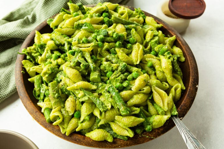 A large wooden bowl filled with green goddess pasta salad including peas, asparagus, and other green vegetables