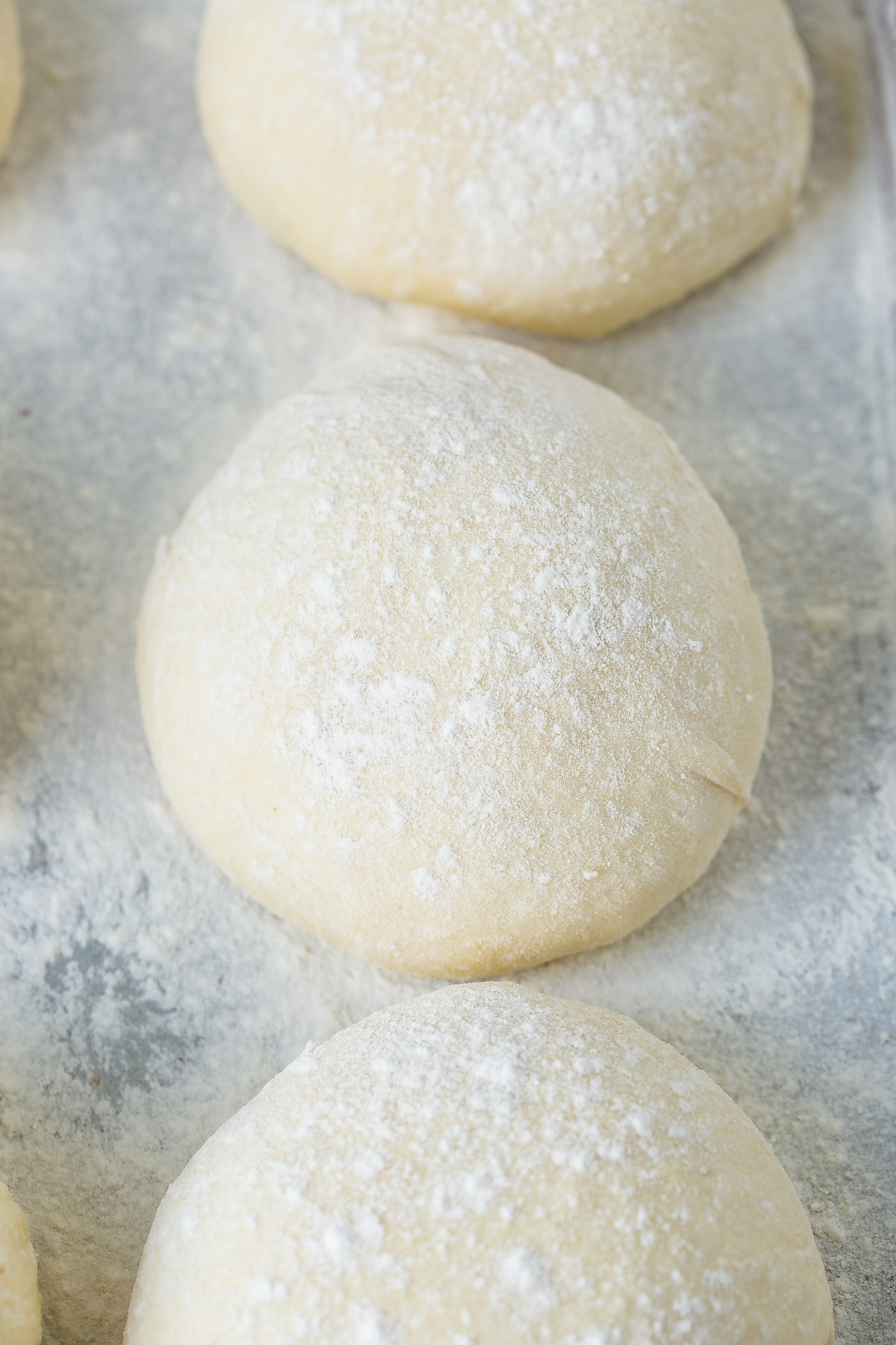 Three balls of pizza dough on a floured cookie sheet.