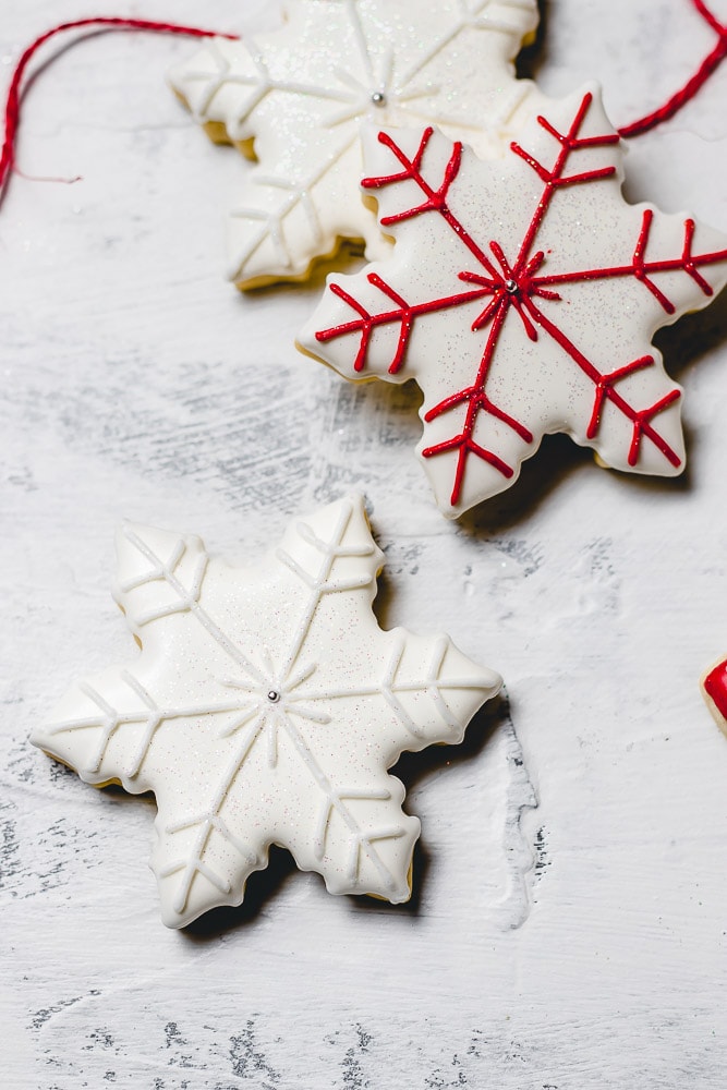 Christmas sugar cookies with royal icing. There are two snow flakes, one has white accents and one has red accents.