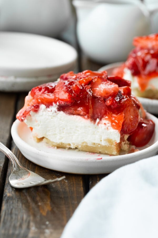 a photo of a square piece of strawberry cheesecake bar sitting on a small dessert plate.