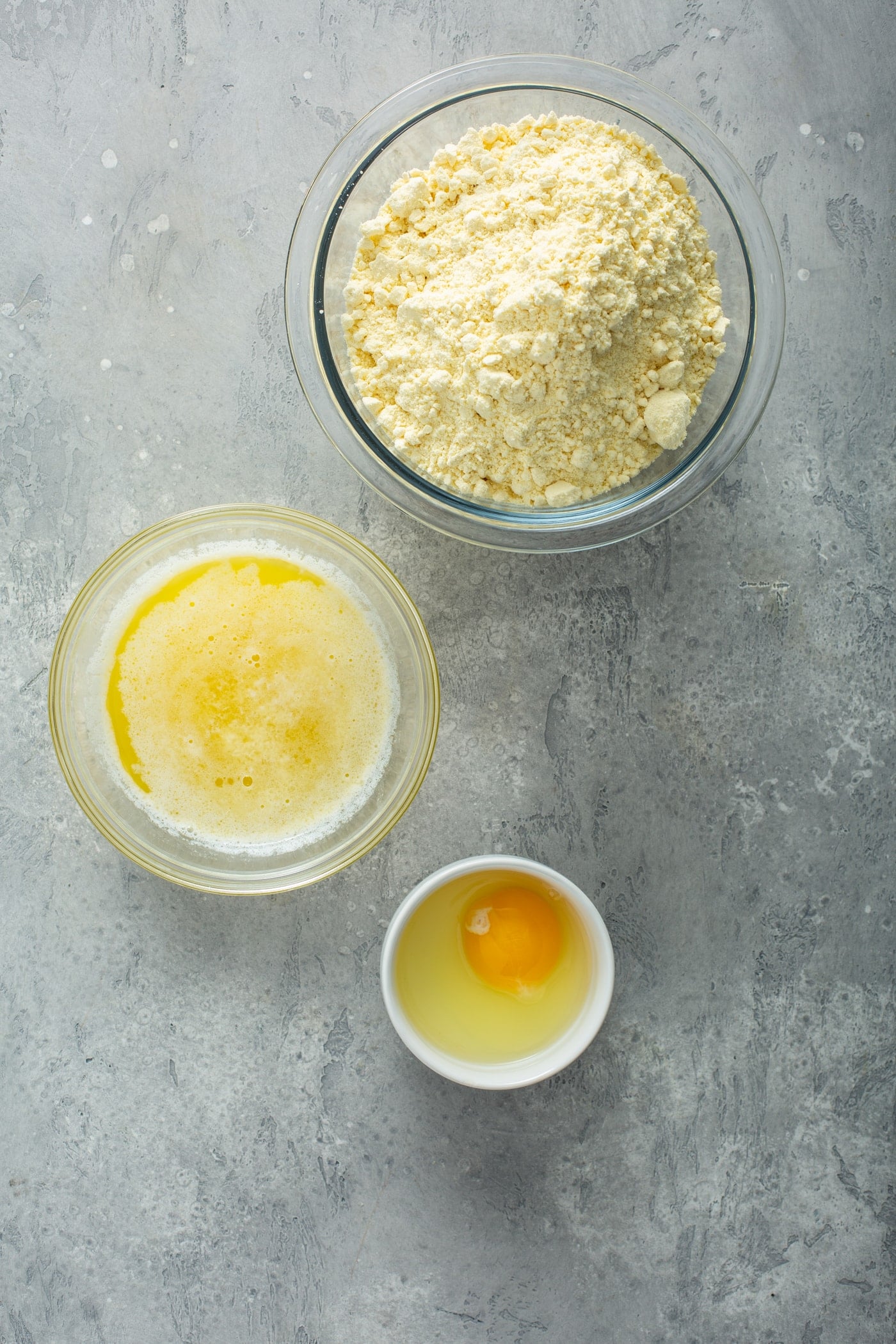 A table holding three bowls containing cake mix, melted butter, and an egg removed from the shell.
