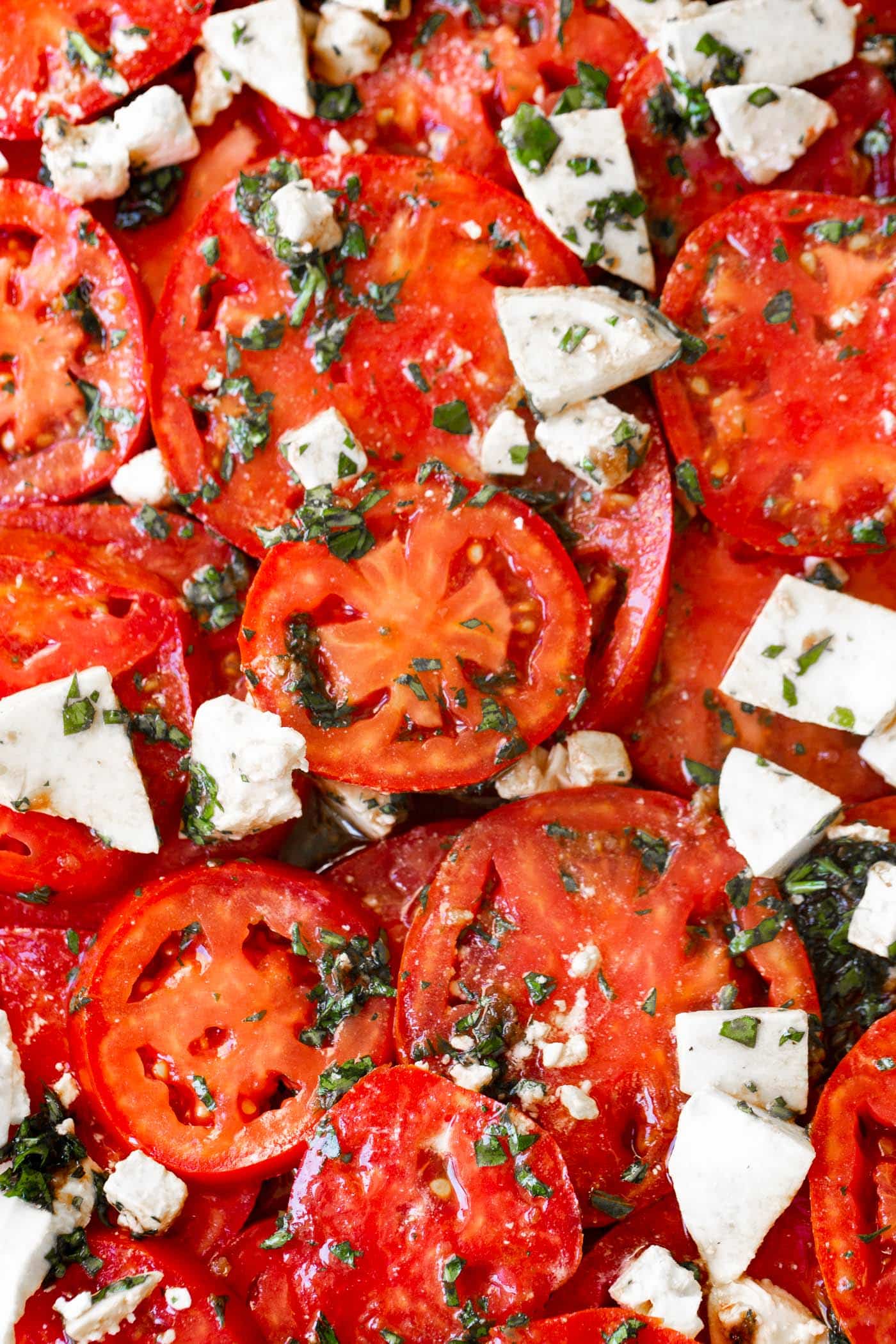 A photo of a marinated tomatoes salad with fresh herbs and 3 cheeses.
