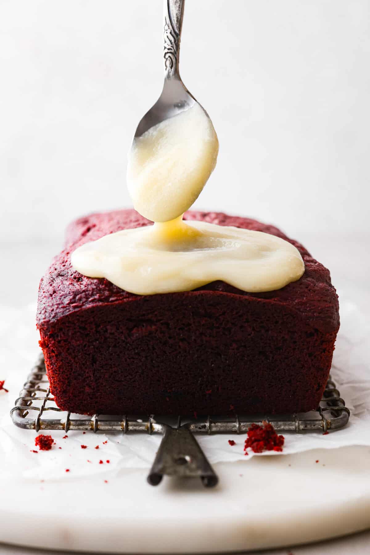 Close side view of the cream cheese glaze drizzling on top of the red velvet pound cake.