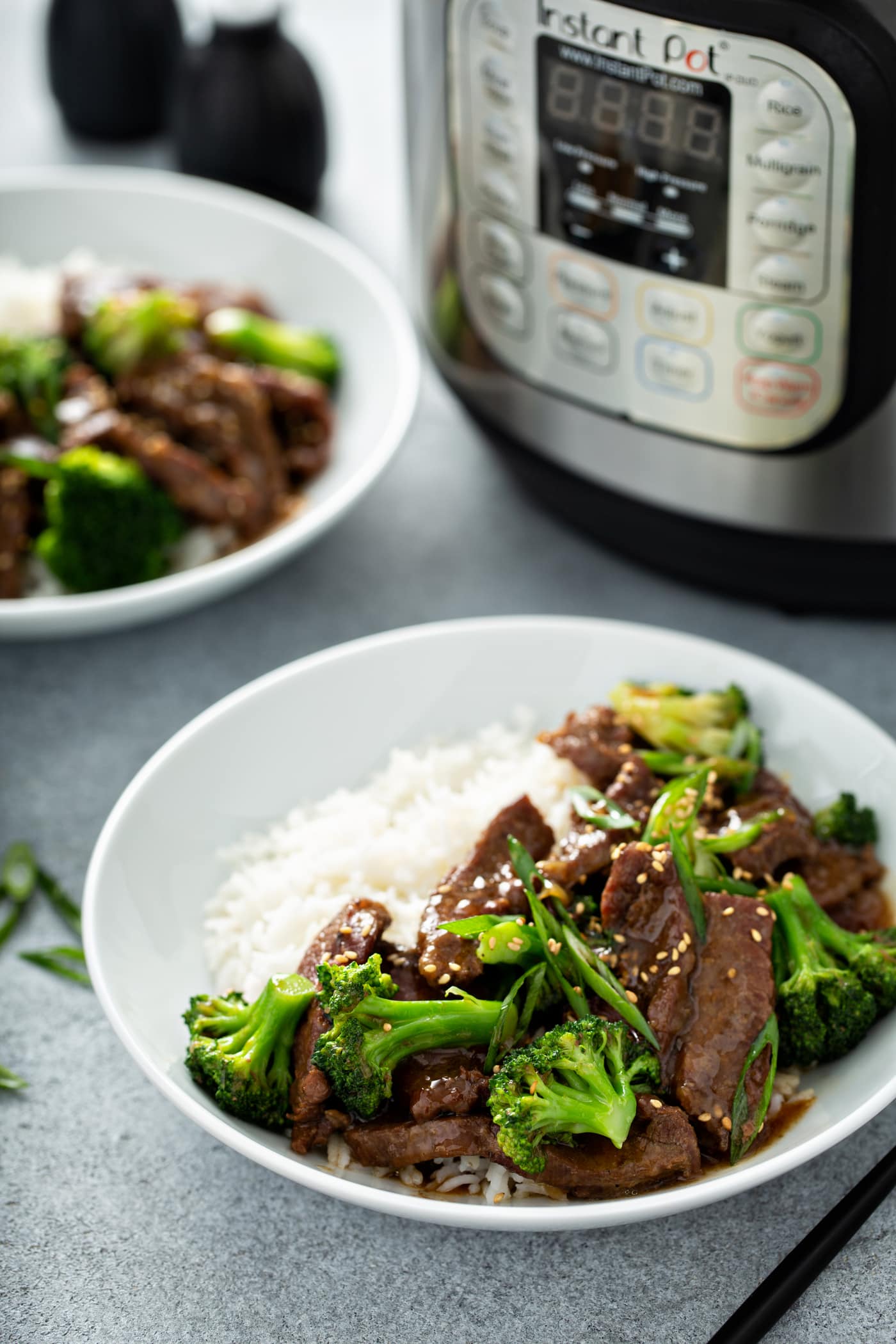 A photo of a white bowl full of beef and broccoli with a side of white rice.