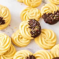 A batch of butter cookies, some chocolate coated, spread over a marble bench top