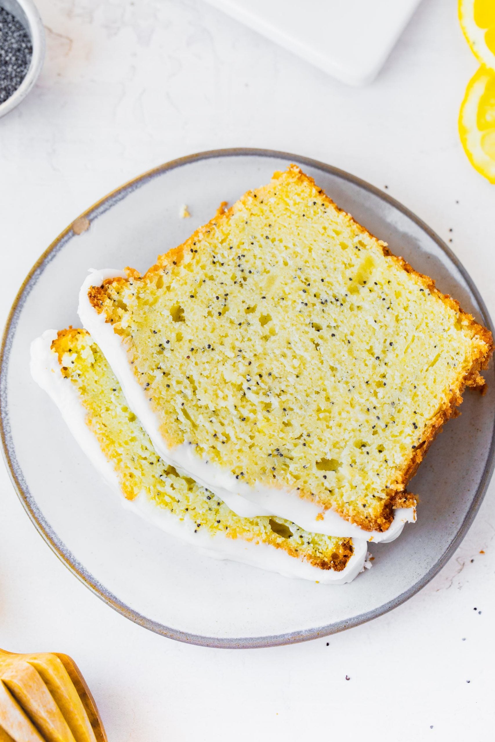 a photo of two slices of lemon poppy seed loaf cake stacked on a plate. the two slices are topped with white icing.