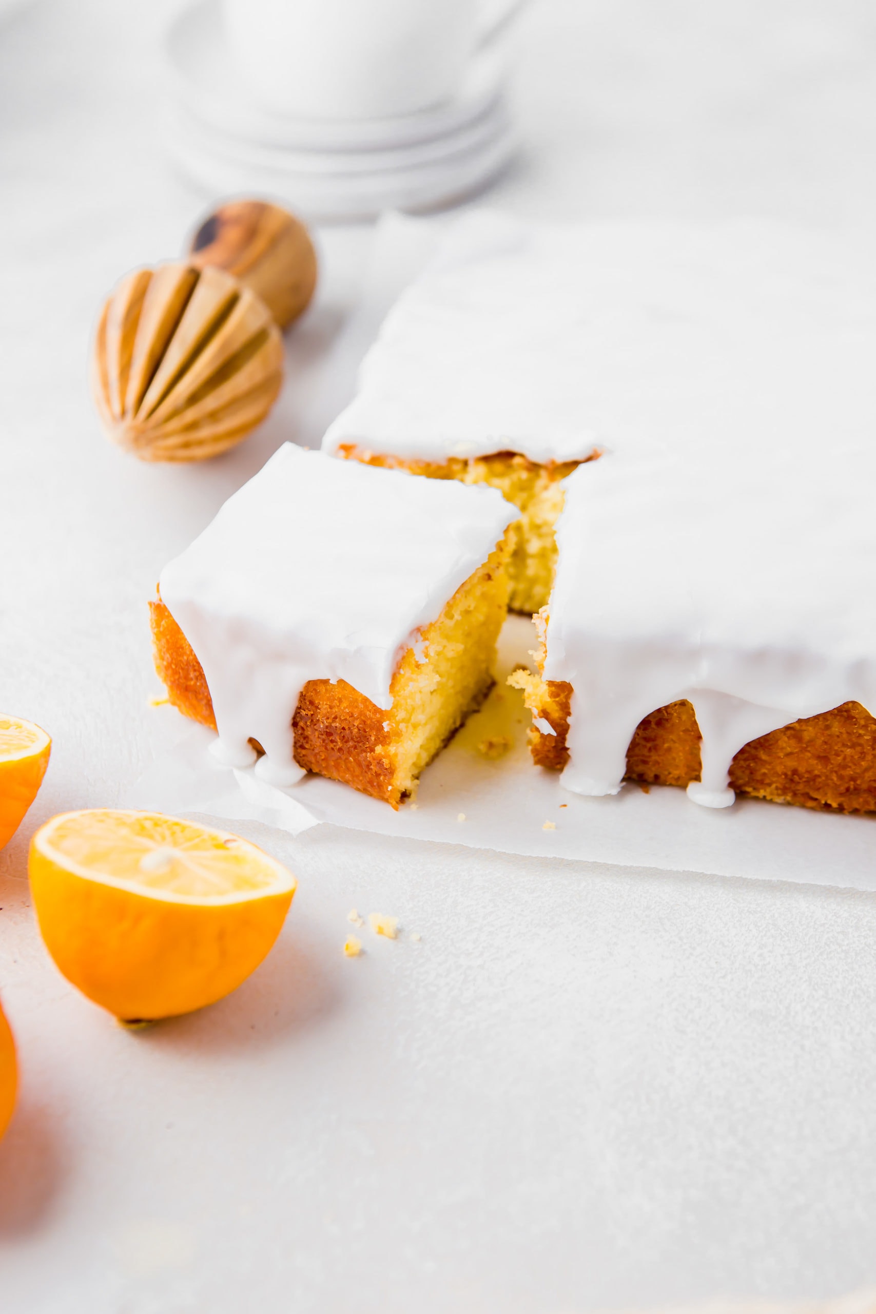 a photo of a square lemon cake covered in a thick white glaze and the corner piece has been cut out and lemon halves are scattered around it.